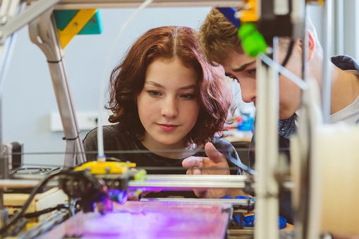 Close up of gen Z teenage girl and boy watching three-dimensional printing in contemporary laboratory.