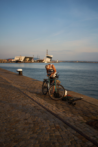 Burgas, Bulgaria - June 17, 2023: a man repairs a bicycle after fishing in the port of Burgas at sunset