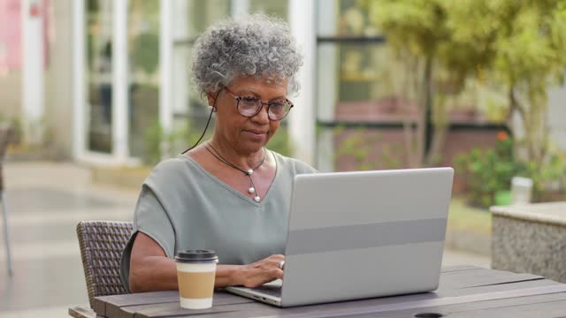 Portrait of senior woman working on laptop outside in coffee shop