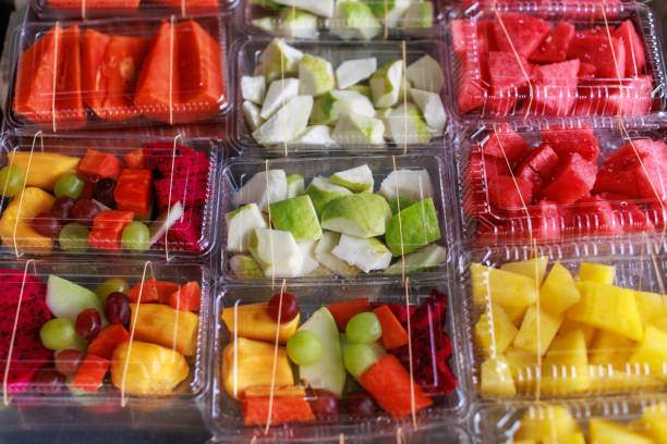Various tropical fruits, cut into small pieces, are arranged and packed in a take-away plastic box, ready for sale at a market stall.