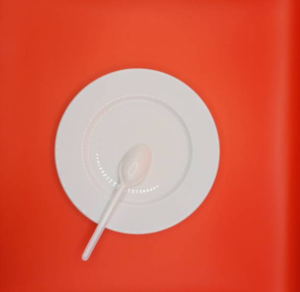 Empty white plate with spoon on red background. Meal preparation concept.