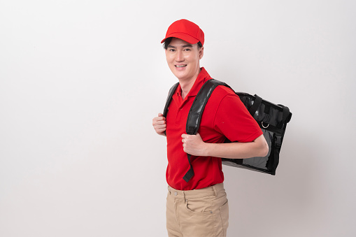 Asian Young food delivery man wearing red uniform carrying food baggage smiling on  white background
