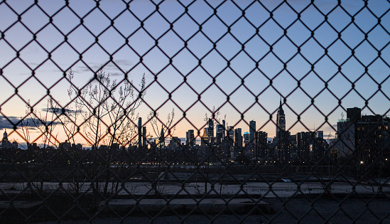 manhattan skyline at sunset view through metal chain link fence (prison, locked away concept) lock fencing separate new york city dusk beautiful