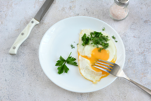 a plate with fried egg and sprig of parsley and a knife on a table