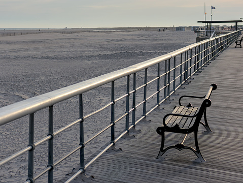 bench on the boardwalk at the beach (jones beach state park on long island nassau county new york) railing with wooden planks and sand (empty, no people) summer relaxation recreation getaway