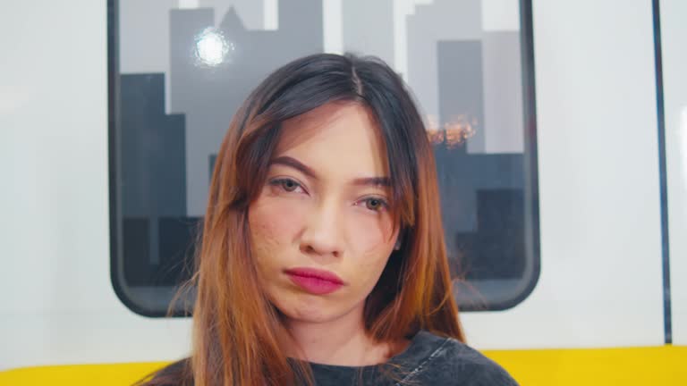 Portrait of a young woman with closed eyes, seemingly daydreaming or relaxing, inside a train with a blurred background.