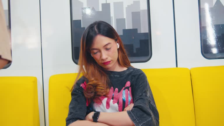 Unhappy young woman sitting with crossed arms on a yellow subway seat, looking away with a displeased expression.