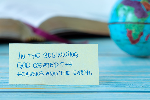 In the beginning God created heavens and earth, handwritten quote with world globe and open holy bible book in the background. Close-up. Christian biblical concept of creation.