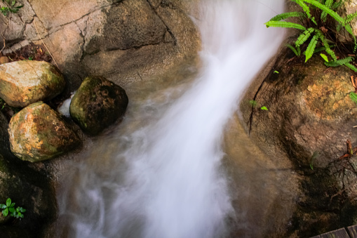 Close-up view of small waterfall into pond in rural in Hong Kong with slow shutter. Waterfall cascading gently over stones in forest. Nature scene.