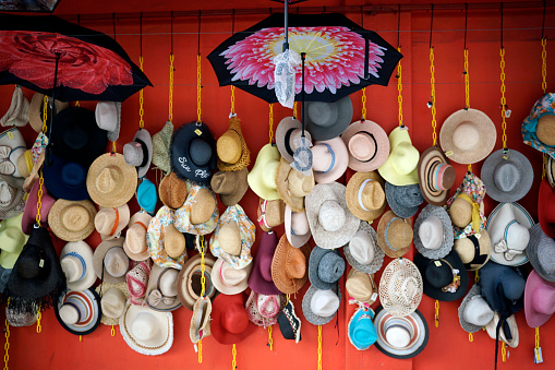 Multiple hats and umbrellas hung on wall for sale at Petaling Street Market in Kuala Lumpur, Malaysia