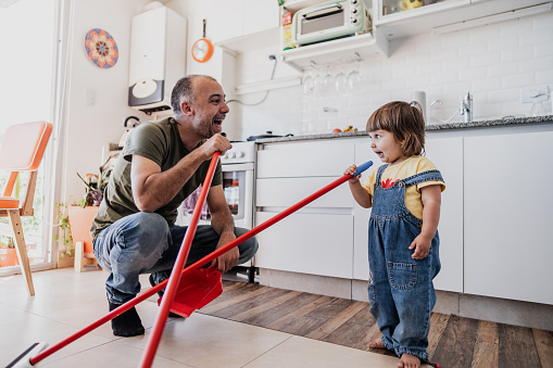 Father and daughter having fun while cleaning the kitchen at apartment