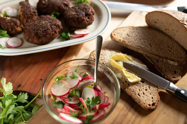 Rustic food. Dinner with fresh fried pork meatballs, sourdough bread, butter and radish salad on wooden table