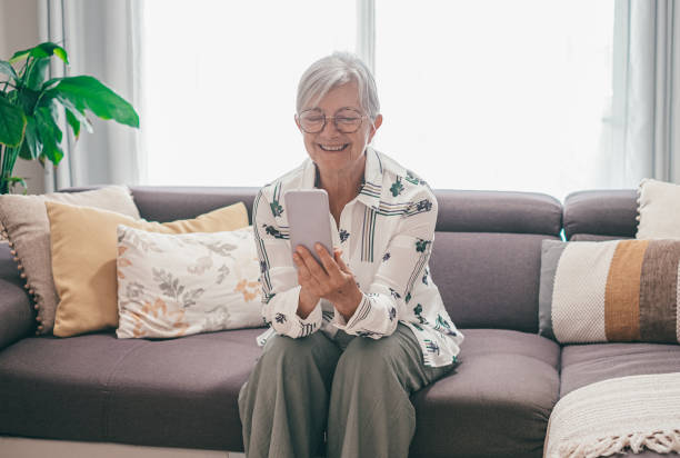 istock Relaxed senior white haired woman sitting on home sofa smiling while using smart phone happy retirement lifestyle in good mood 2148718984