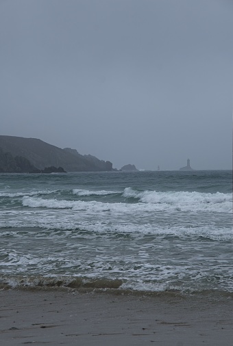 Wonderful landscapes in France, Brittany. Baie des Trepasses Beach in Plogoff. Surfers and Old Lighthouse (Phare de la Vieille). Cloudy spring day. Selective focus