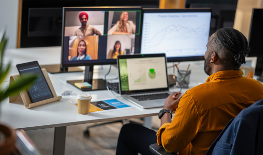 Rear view of a businessman of African descent talking with colleagues during a video conference at his desk at home office. Business and career concept.
