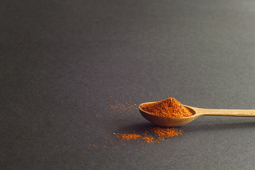 A wooden spoon with hot milled pepper on a dark background. Dark background with blank space for text.