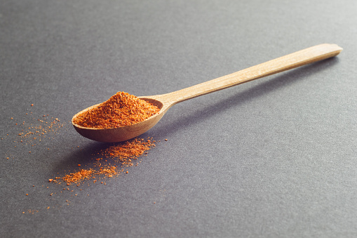 A wooden spoon with hot milled pepper. Dark background