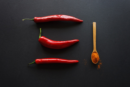Still life of pods of hot pepper and a spoon with milled pepper on a dark background. Culinary concept.