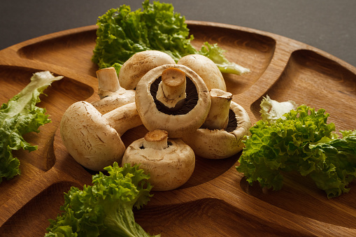 Leaves green salad and champignons on a wooden plate