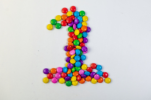 A single, colorful candy shaped like the number one rests on a clean white background