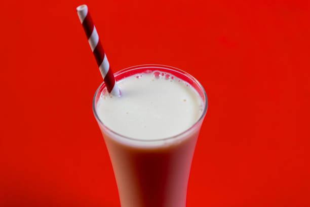 A refreshing milkshake in a glass with a straw, set against a vibrant red background.