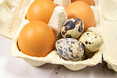 A carton of chicken eggs with a few quail eggs in it