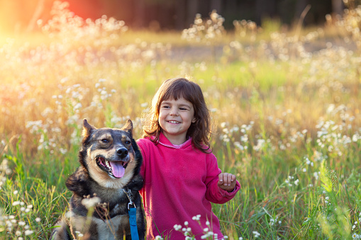 Happy Little girl with a dog walking in the flower field in spring
