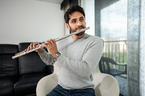 Mid adult man playing the flute at home