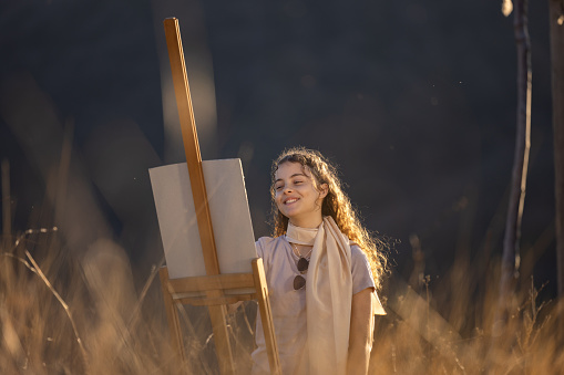 Happy teenage girl painting in nature during sunset