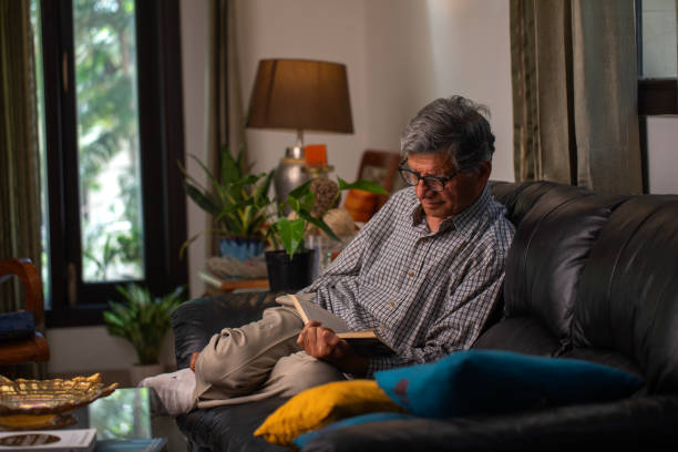 Senior man reading book on comfortable sofa at home