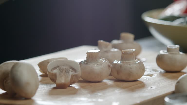 cook cuts several champignons in half on the kitchen board at once