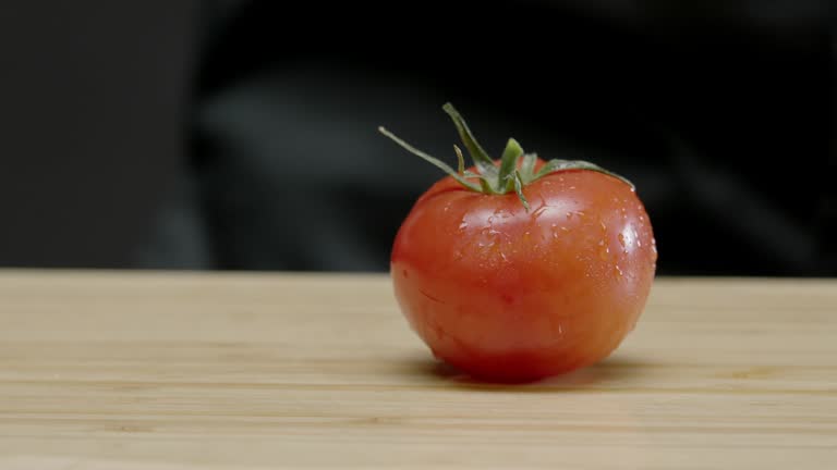 chef places a delicious, ripe, washed tomato on the cutting board.