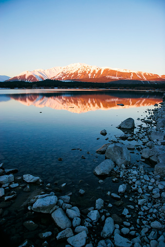 At Lake Tekapo, the sunset ignites the land offering a striking display of vibrant colors painting the sky. As the sun dips below the horizon, hues of clear blue run across the landscape. The tranquil waters of the lake reflect the celestial spectacle, enhancing the picturesque scene. Visitors often gather along the lakefront to witness this natural phenomenon, which occurs regularly in the evenings, creating a serene ambiance conducive to reflection and appreciation of nature's beauty.