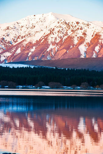 At Lake Tekapo, the sunset ignites the land offering a striking display of vibrant colors painting the sky. As the sun dips below the horizon, hues of clear blue run across the landscape. The tranquil waters of the lake reflect the celestial spectacle, enhancing the picturesque scene. Visitors often gather along the lakefront to witness this natural phenomenon, which occurs regularly in the evenings, creating a serene ambiance conducive to reflection and appreciation of nature's beauty.