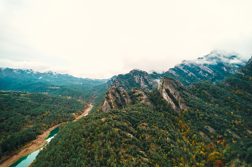 A picturesque natural landscape with a river winding through mountains and forests, under a clear sky with fluffy clouds