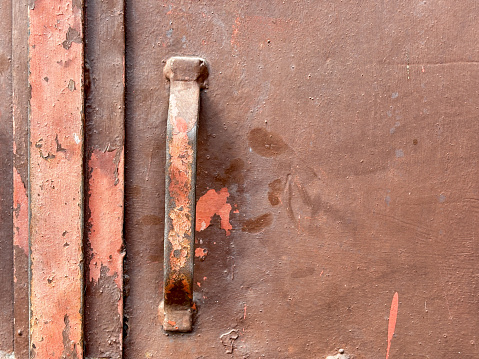 A rusty metal handle is on a brown surface. The handle is rusted and has a worn appearance