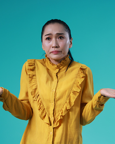 Studio shot A woman spreads her hands shrugs her shoulders careless ignorance expression, uncertain facial expression isolates the blue sky  color background