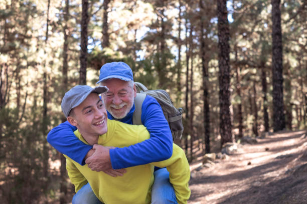 istock Grandson carries his grandfather on shoulders during excursion day in forest. Smiling multi-generational family couple enjoying mountain and nature together. New generation care and helps the old one 2148730416