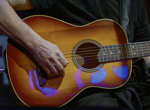 Image of a guitarist's hand playing on the strings of a guitar