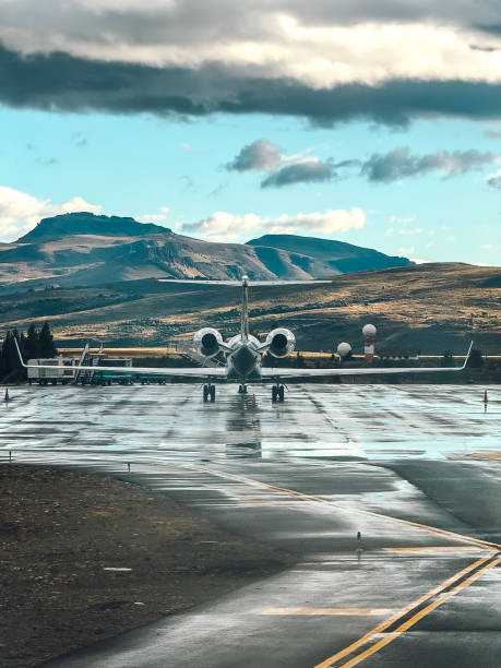 A small jet plane is sitting on the runway in front of a mountain range. The sky is cloudy and the plane is ready for takeoff