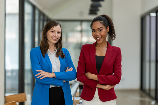 Two diverse businesswomen standing back-to-back, projecting confidence and partnership in a modern office space.
