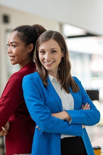Two diverse businesswomen standing back-to-back, projecting confidence and partnership in a modern office space.