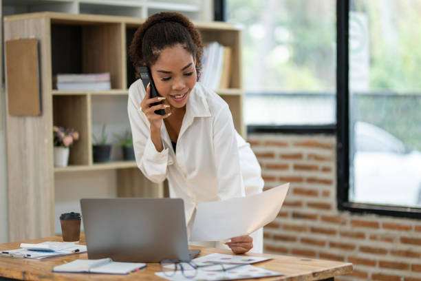 istock Young professional woman engaged in a phone conversation while working on her laptop at an organized office desk. 2148731535