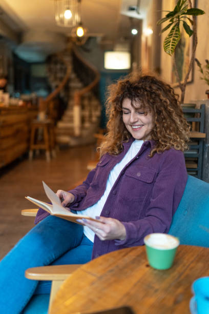istock Young woman drinking coffee and reading a book in a cafe 2148732409