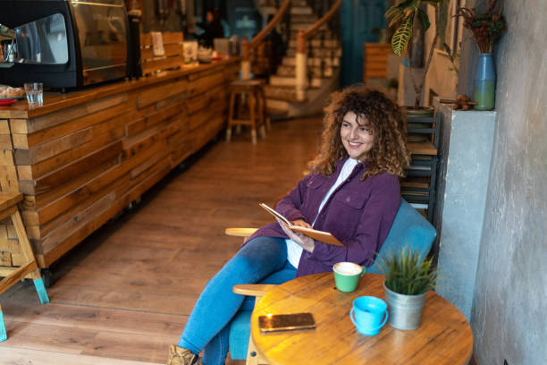 Young woman drinking coffee and reading a book in a cafe