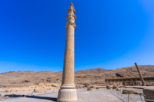 A towering column adorned with intricate carvings stands against the clear blue sky at Persepolis. Captures the essence of ancient Persian architecture. Persepolis, Iran.