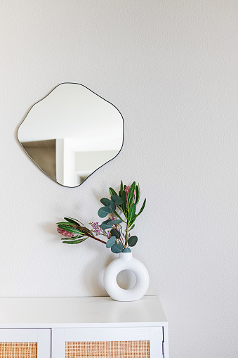 Minimalist home decor. Sandstone donut-shape vase on the dresser and organic fluid shape mirror on the wall