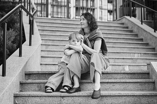 Happy family: mother and child son hugging and laugh sitting on the city stairs. motherhood concept, togetherness, love emotion. Urban city concept, residential complex in Ukraine. High quality photo