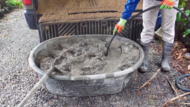 Worker uses a hose to add water to a basin and Mixing Cement and Sand, Construction Site and Building Materials concept.