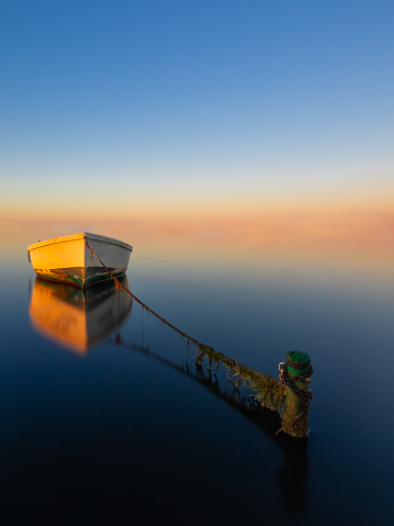 Boat anchored on the beach at sunset with an infinite sky. Fishing concept.